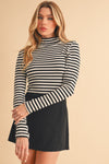 A woman wearing a black and white striped turtleneck top paired with a black skirt.