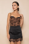 Woman wearing a black lace top and skirt against a beige background