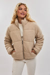 Woman wearing a beige quilted jacket against a plain background