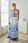Woman wearing a white dress with blue floral patterns in a bright room.