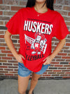 Person wearing a red 'Huskers Volleyball' t-shirt in front of a brick wall