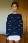 Woman wearing a navy blue sweater with white stripes and white shorts indoors.