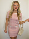 Woman wearing a pink dress holding a beige handbag against a plain background