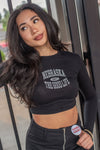A woman wearing a black long sleeve crop top with the text 'Nebraska' on it, paired with black pants.