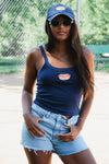 Woman wearing a blue tank top and denim shorts with a cap and sunglasses outdoors.