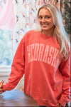 Person wearing a red 'NEBRASKA' sweatshirt in a room with colorful curtains.