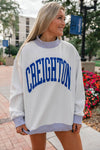 Woman wearing a white sweatshirt with 'Creighton' printed on it, standing outdoors.