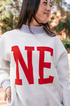 Person wearing a white sweatshirt with red 'NE' letters outdoors.
