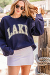 Woman wearing a navy sweatshirt with 'LAKE' text, standing by a wooden post.