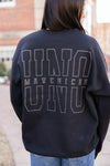 Person wearing a black sweatshirt with 'UNO Mavericks UNO' text on the back, standing outdoors.