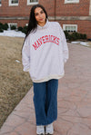 Person wearing a 'Mavericks' sweatshirt standing on a stone path in front of a brick building.