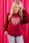 Woman wearing a red sweatshirt with a heart design against a pink curtain background
