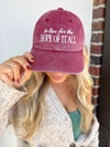 Person wearing a maroon cap with text, holding it up to their face.